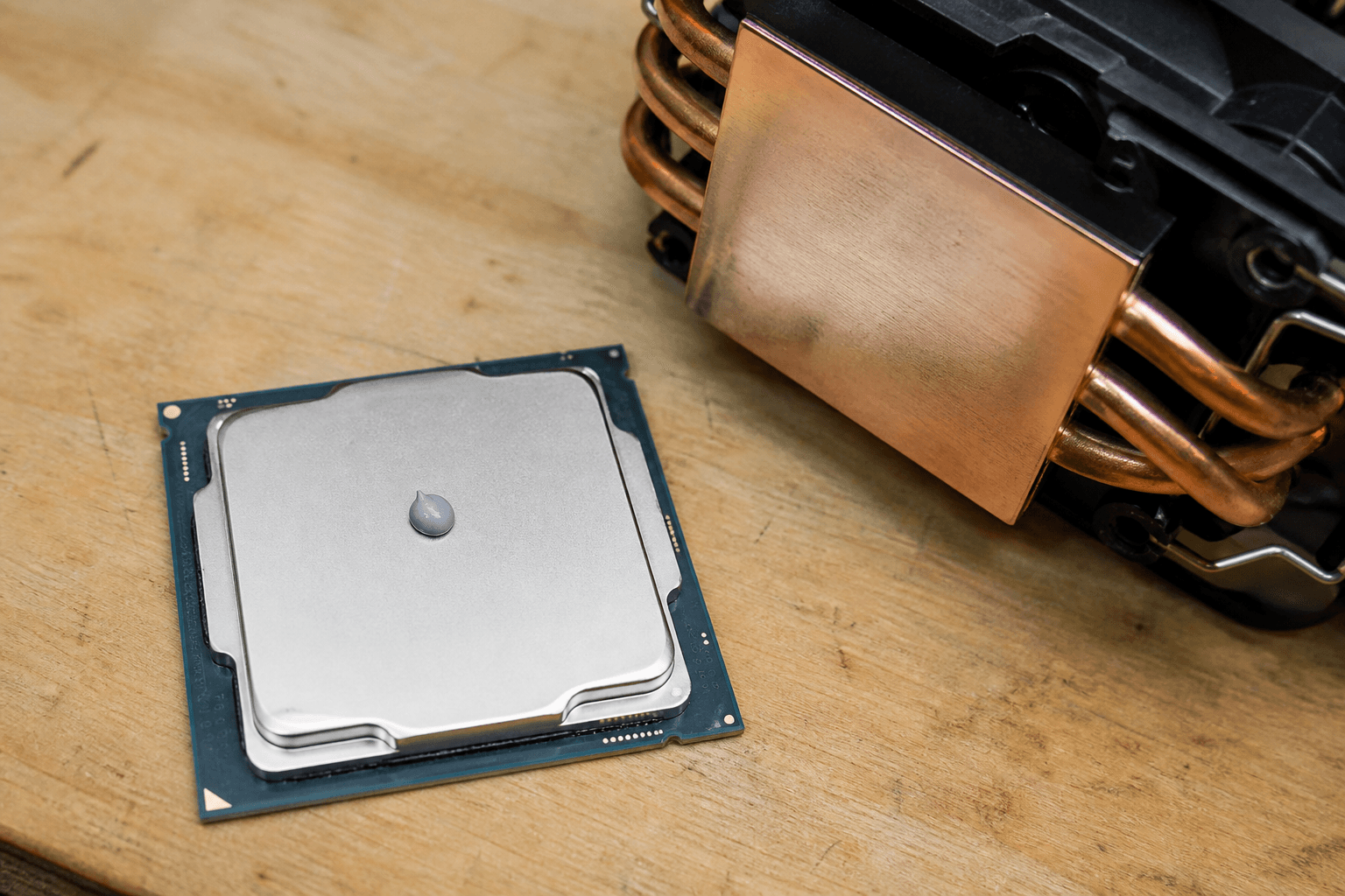CPU-Kühler liegt neben einem Prozessor, kleine Menge Paste auf dem Heatspreader