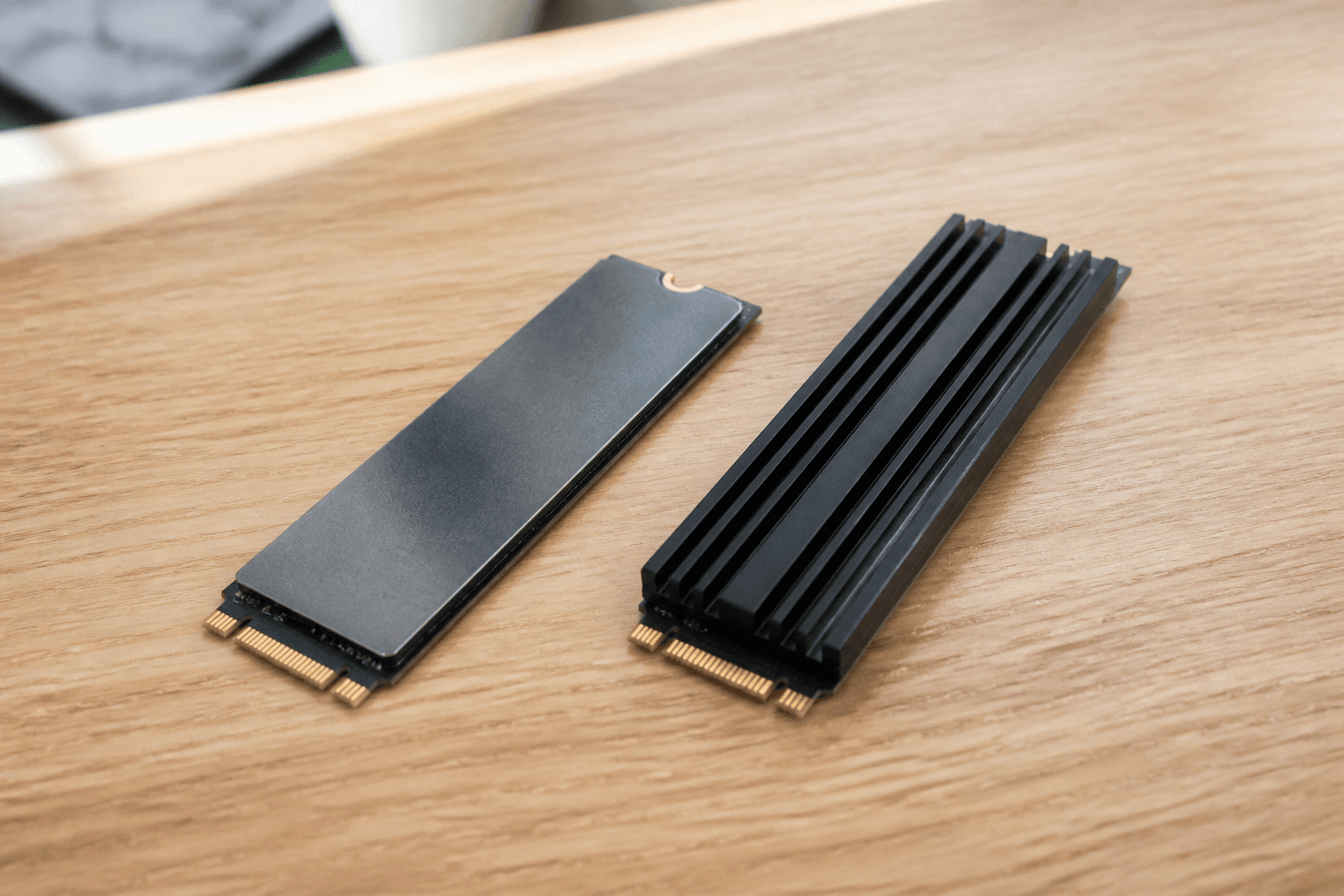 Zwei M.2-SSDs nebeneinander auf einem Holztisch, eine mit Kühlkörper